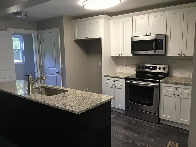 Modern kitchen with white cabinets, stainless steel appliances, granite countertops, and dark gray island.