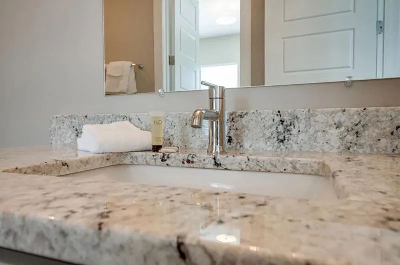 Bathroom sink with granite countertop and stainless steel faucet, with mirror and towel.