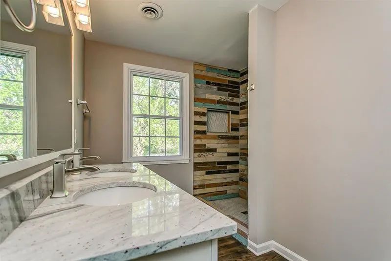Bathroom with a dual-sink vanity, window, and a shower with wood-look tile.