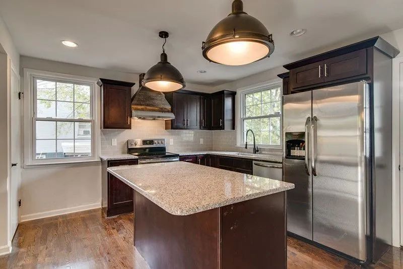Modern kitchen with dark wood cabinets, stainless steel appliances, and granite island countertop.
