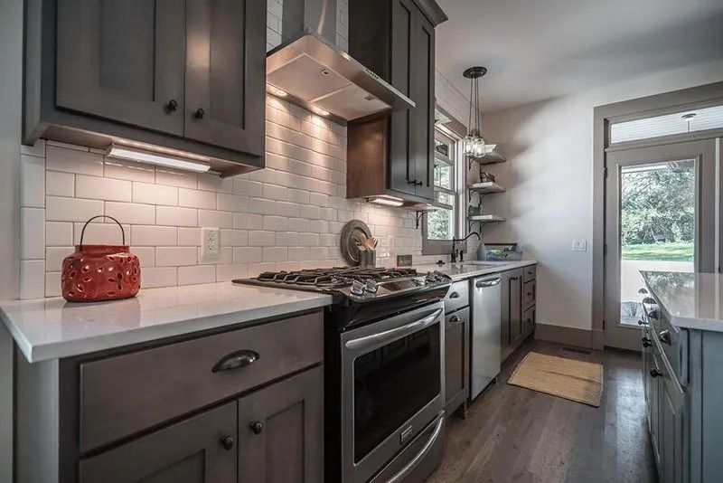 Kitchen with grey cabinets, white tile backsplash, stainless steel appliances, and white countertops.