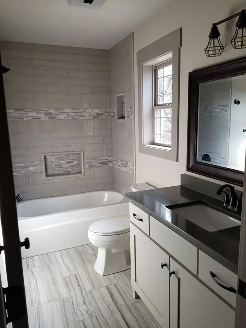 Newly remodeled bathroom with grey and white tiles, tub, vanity, and toilet.