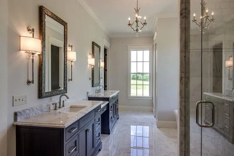 Bathroom with dark vanities, white countertops, large mirrors, glass shower, and chandelier.