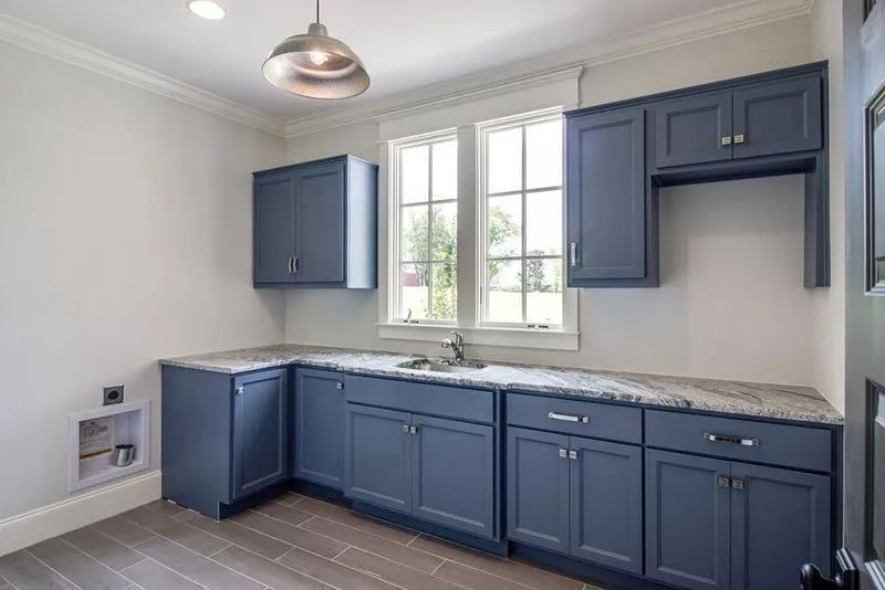 Blue cabinetry and light fixtures in a laundry room with a window, countertop, and sink.