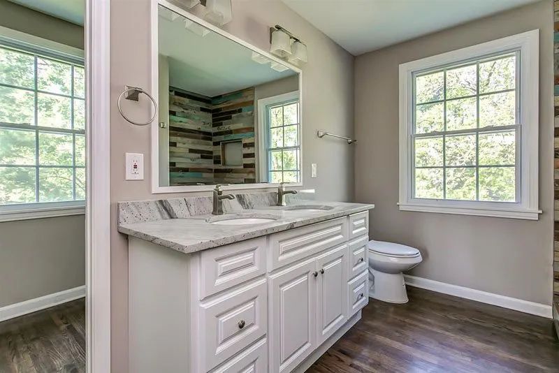 Bathroom with white vanity, gray countertop, large mirror, two windows, and toilet.
