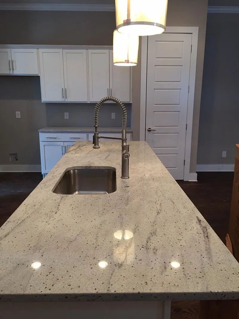 Kitchen island with granite countertop, sink, and faucet. White cabinets and pendant lights in background.