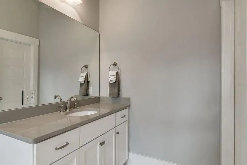 Bathroom with white vanity, gray countertop, and large mirror. Gray walls and a towel ring.