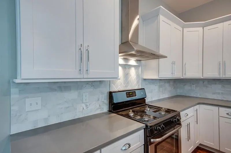 White kitchen cabinets above a stove, with gray countertops and backsplash.