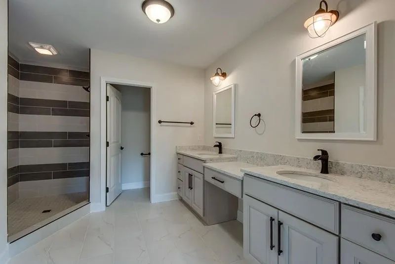 Spacious bathroom with gray vanities, white countertops, and a shower with horizontal gray tile accents.