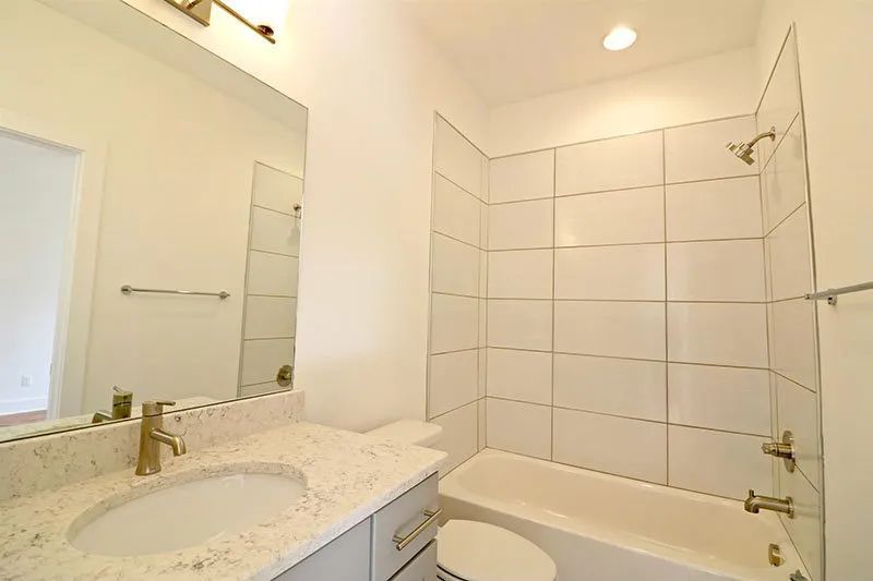 Bathroom with white tiled walls, a vanity with a granite countertop, and a bathtub.