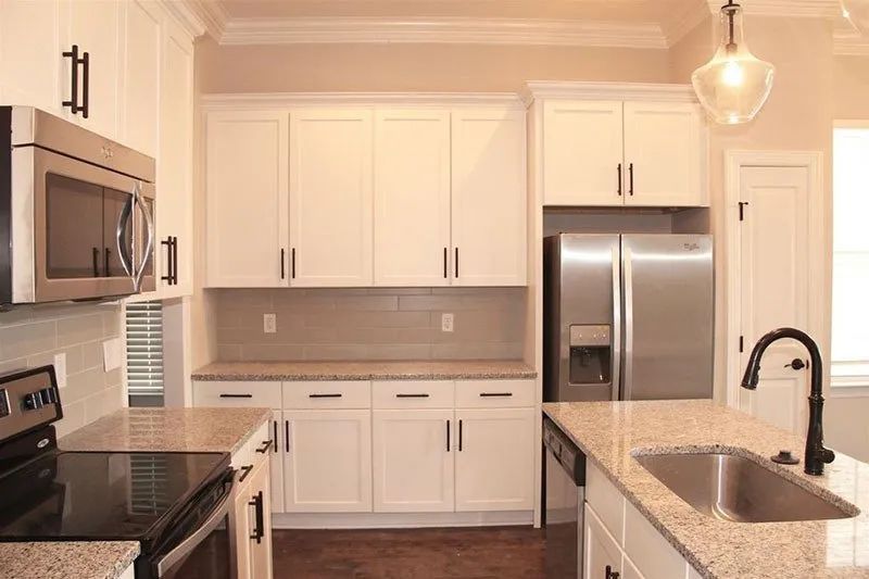 White kitchen with stainless steel appliances, granite countertops, and dark cabinet hardware.