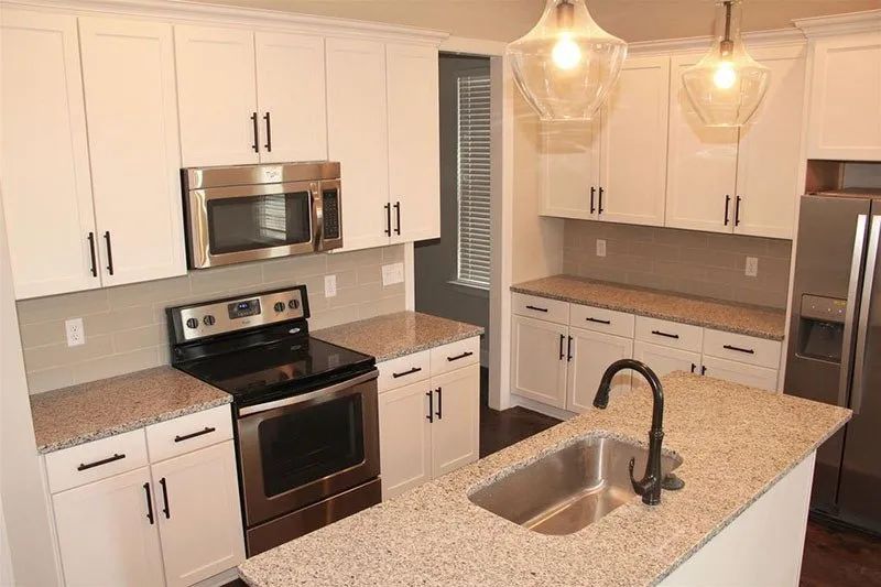 White kitchen with stainless steel appliances, granite countertops, and two pendant lights.