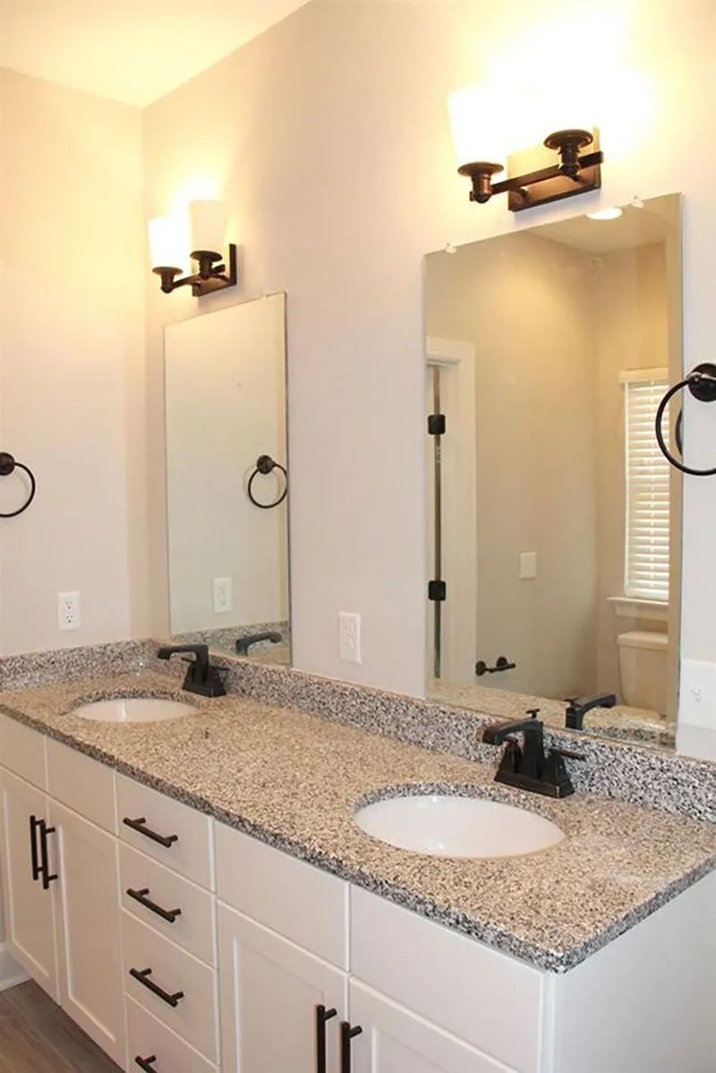 Bathroom with double vanity, granite countertop, two mirrors, and black fixtures.