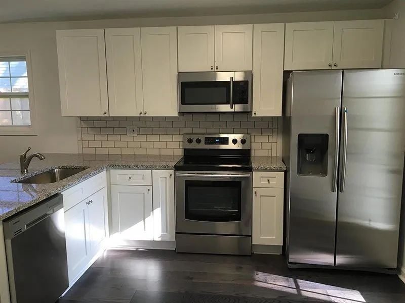Modern kitchen with white cabinets, stainless steel appliances, and dark gray countertop.