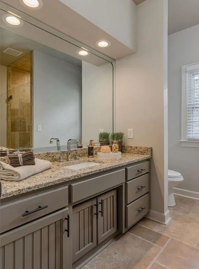 Bathroom with a double vanity, large mirror, granite countertop, light gray cabinets, and a nearby toilet.