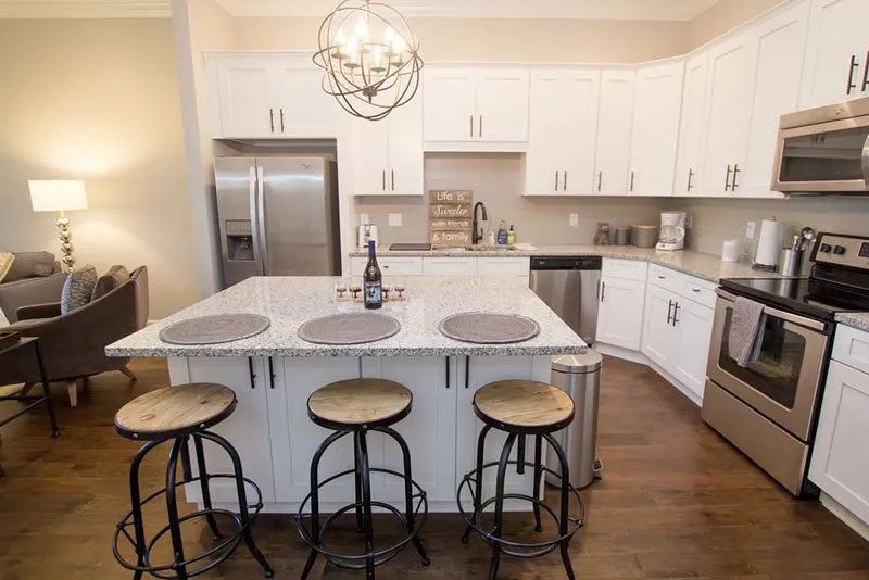Modern kitchen with white cabinets, stainless steel appliances, and a granite island with stools.