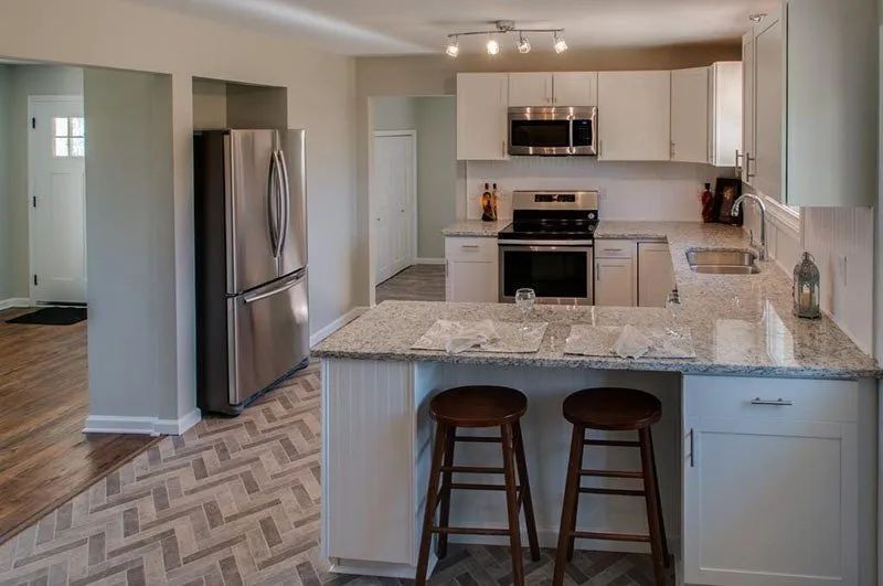 Modern kitchen with white cabinets, stainless steel appliances, and a granite countertop island with two stools.