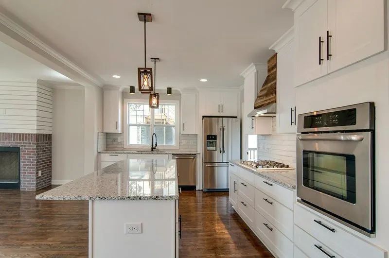 White kitchen with granite countertops, stainless steel appliances, and wood flooring.