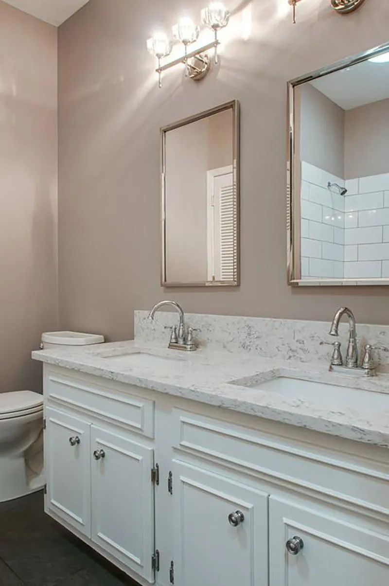 Bathroom with white vanity, marble countertop, silver fixtures, two mirrors, and a toilet.