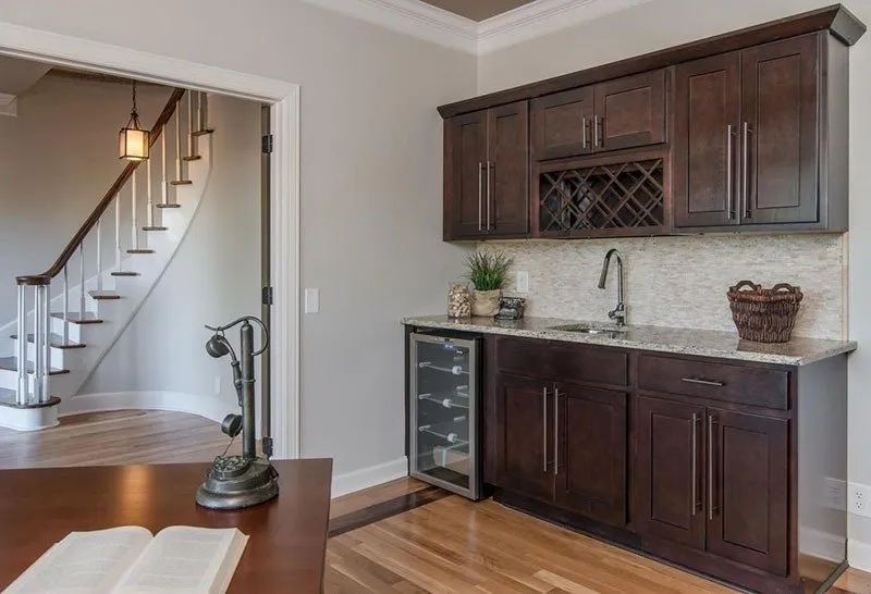 Home bar area with dark wood cabinets, a wine cooler, and a staircase in the background.