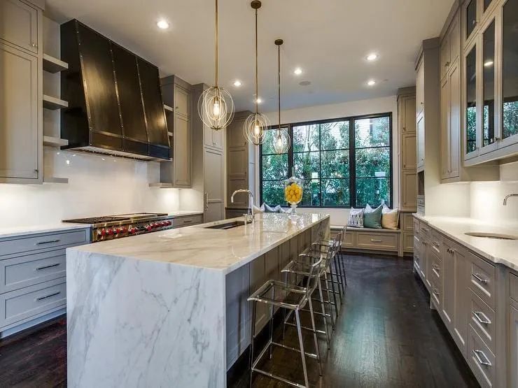 Elegant kitchen with marble island, stainless range hood, gray cabinets, and clear bar stools.