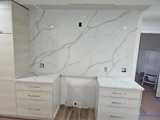 Kitchen remodel with white marble-like backsplash, countertops, and light cabinets.