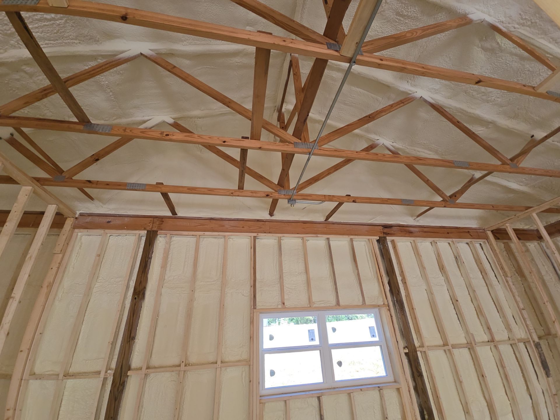 Interior view of a building with wooden frame and spray foam insulation on walls and ceiling.