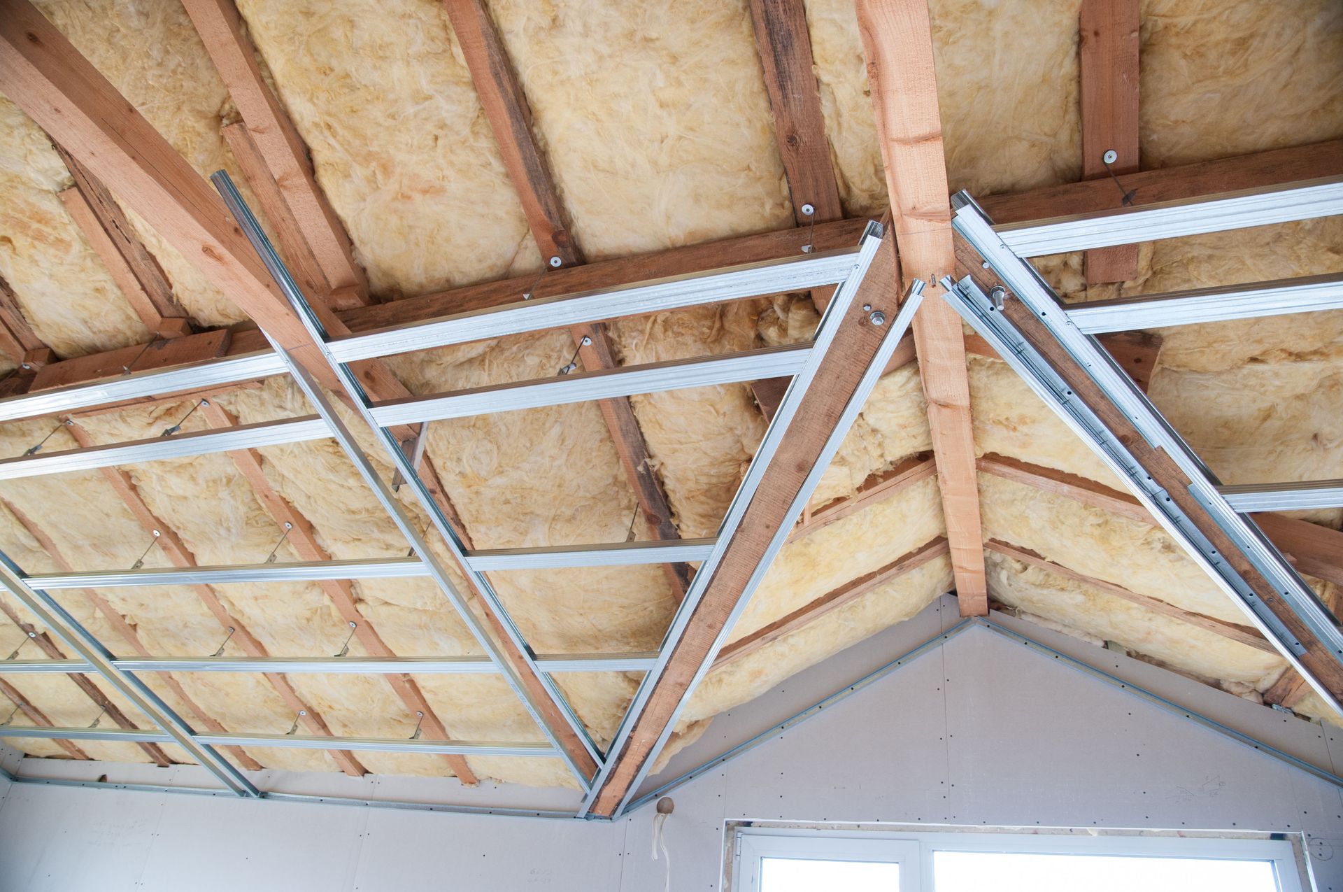 Interior view of attic under construction, showing insulation between wooden rafters and metal framework.