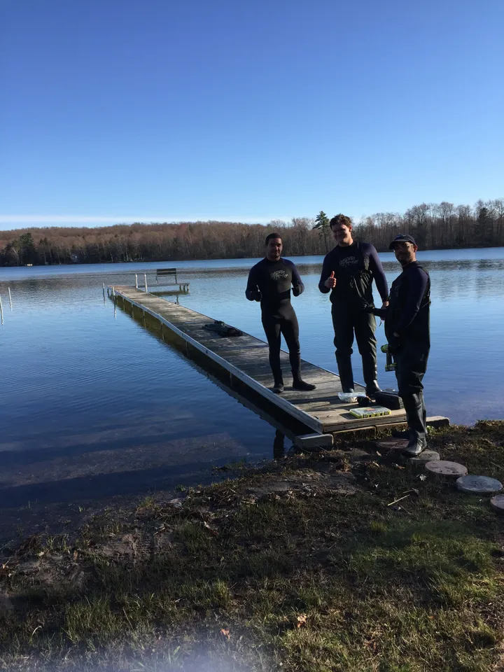 three people are standing on a dock next to a lake