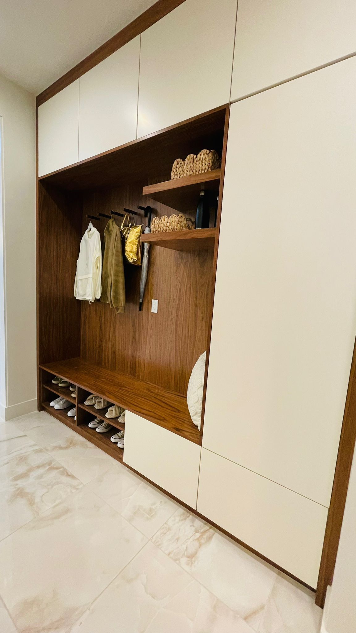 Modern entryway storage unit with white cabinets, wood shelving, a hanging rack for clothes, and open shoe storage.