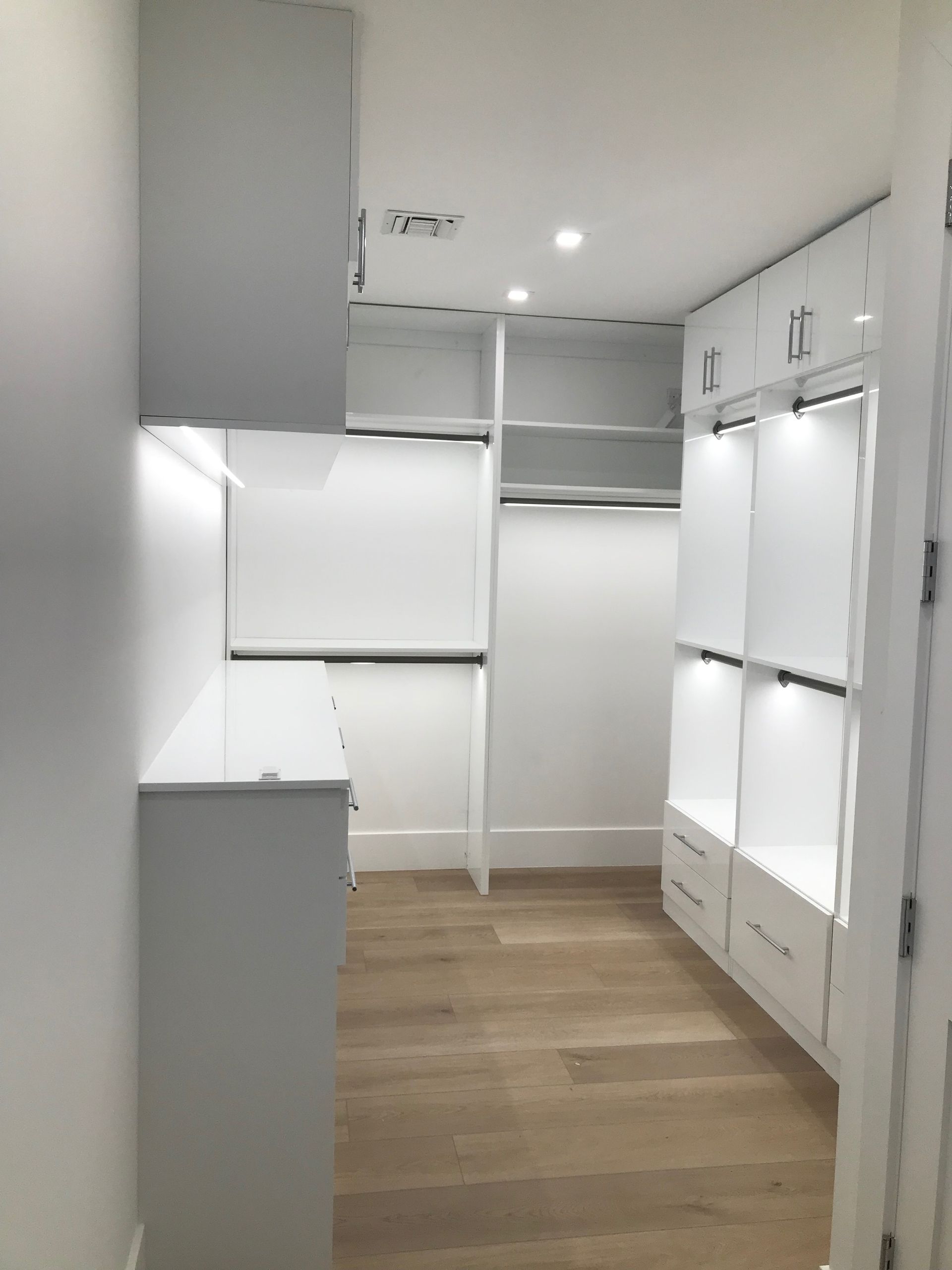 A modern walk-in closet featuring white cabinets, integrated LED lighting, and light wood-tone flooring.