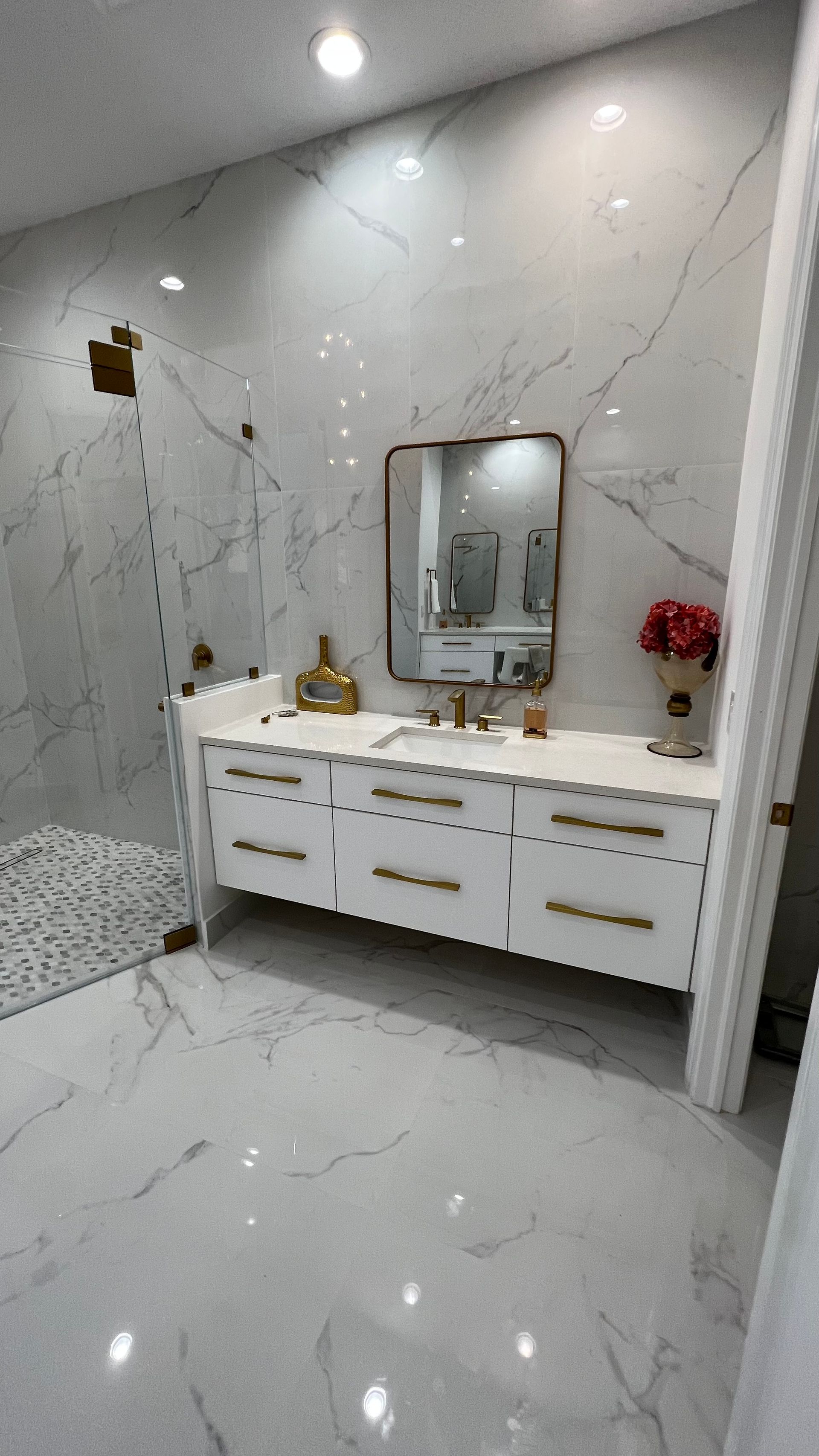 Modern white marble bathroom with a double vanity, gold hardware, and an open shower area.