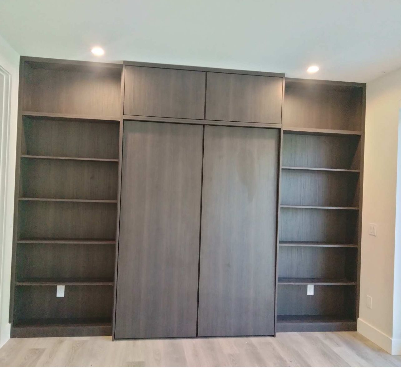 Built-in floor-to-ceiling dark wood shelving unit with a central cabinet featuring two tall doors.