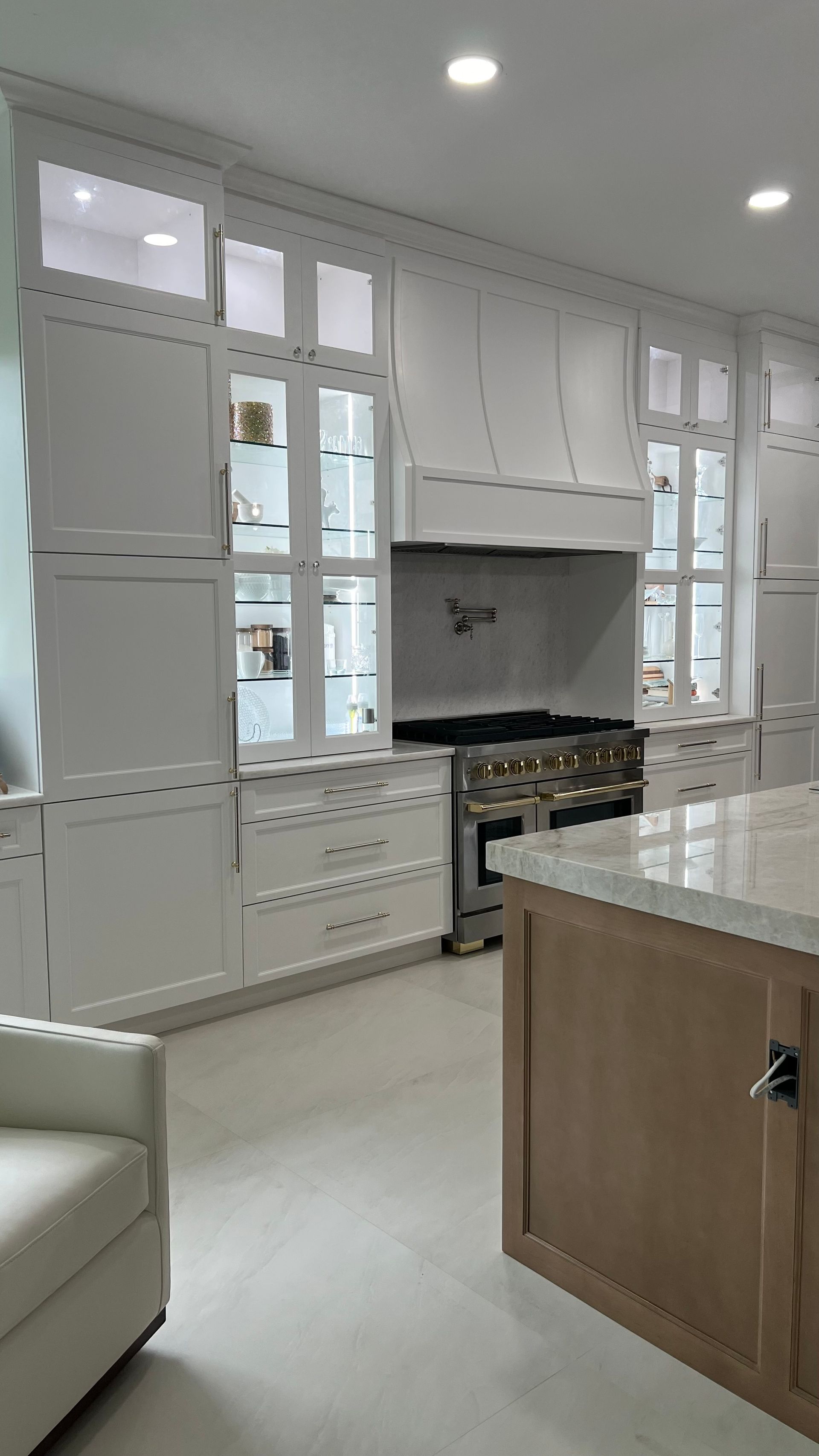 A modern, bright kitchen features white cabinets with glass display doors, a professional stove, and a wood island.