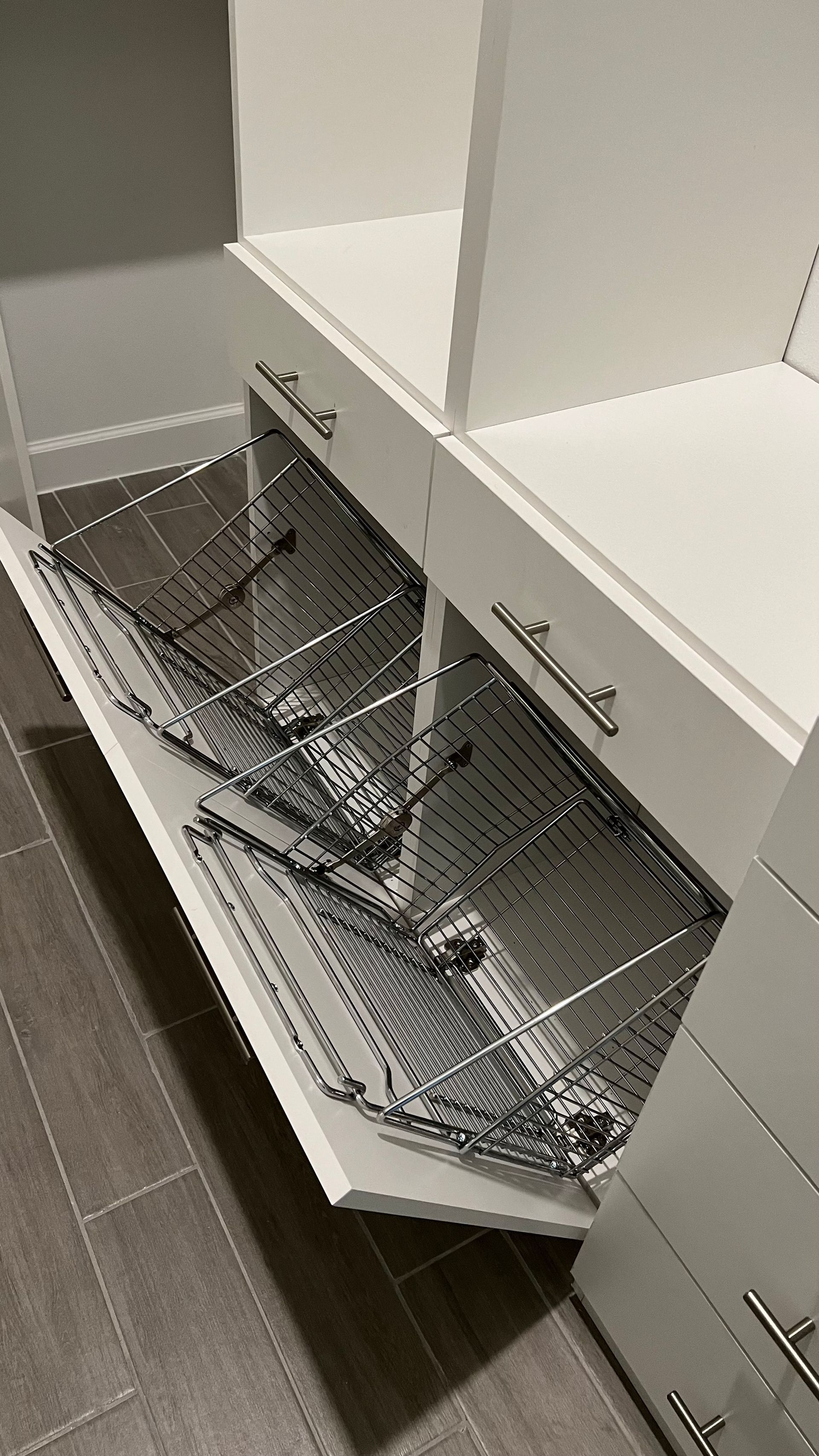A white closet cabinet with two pull-out metal wire storage baskets extended on a tiled floor.