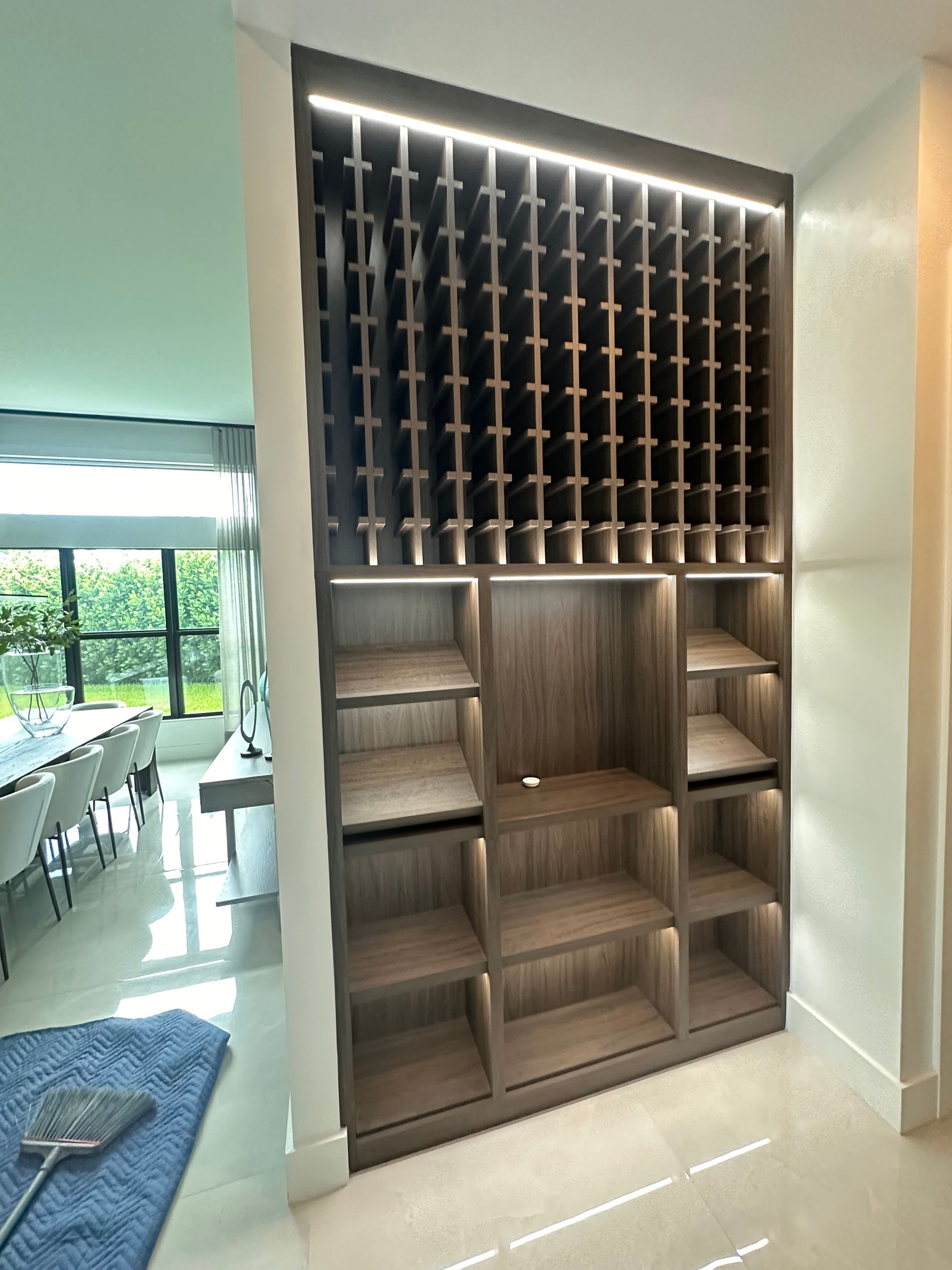 A dark wood floor-to-ceiling built-in wine rack with illuminated grid shelving and open display shelves below.