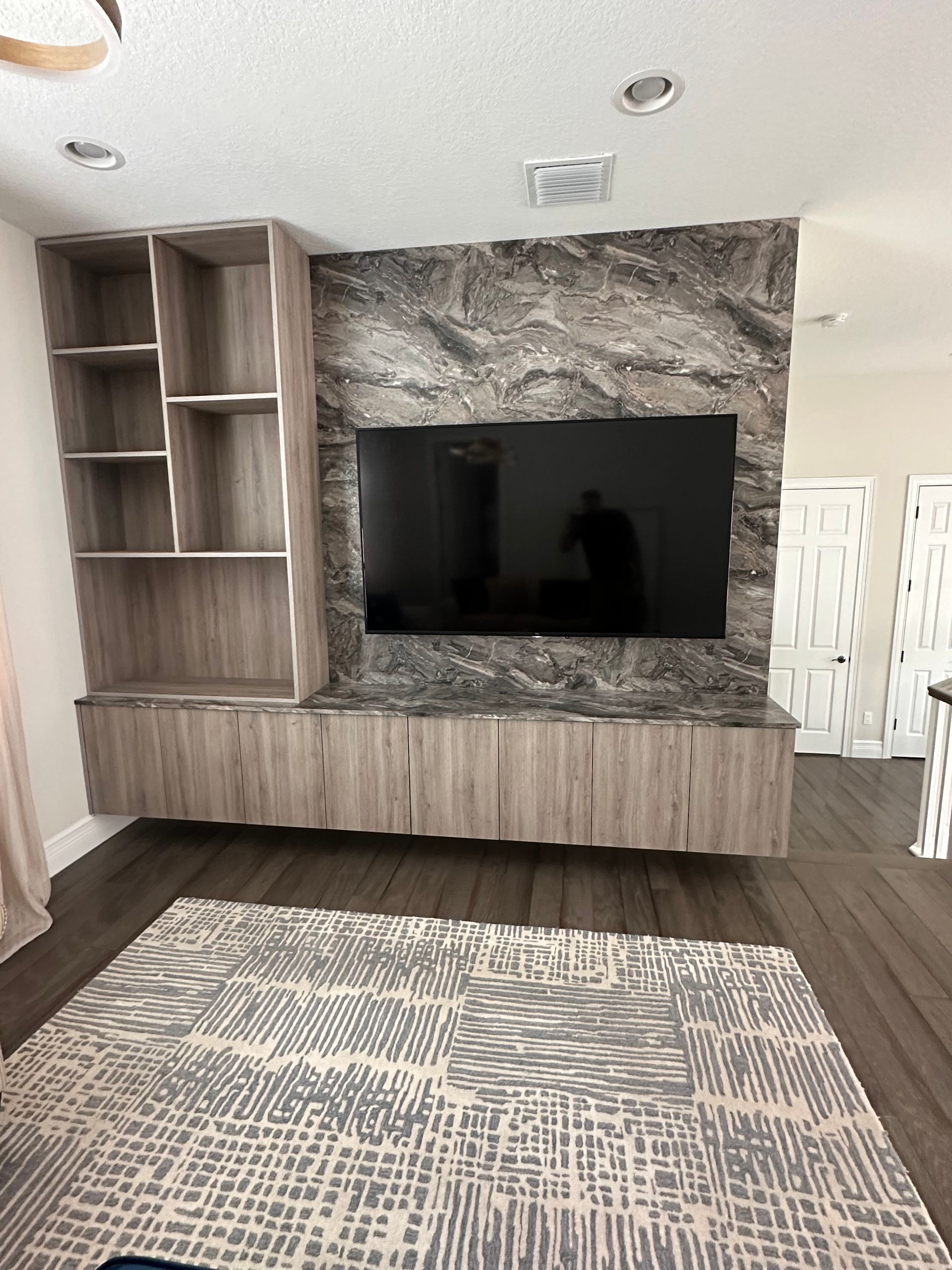 A living room wall with a wall-mounted TV on a grey stone feature, wood shelving, and a matching floating console.
