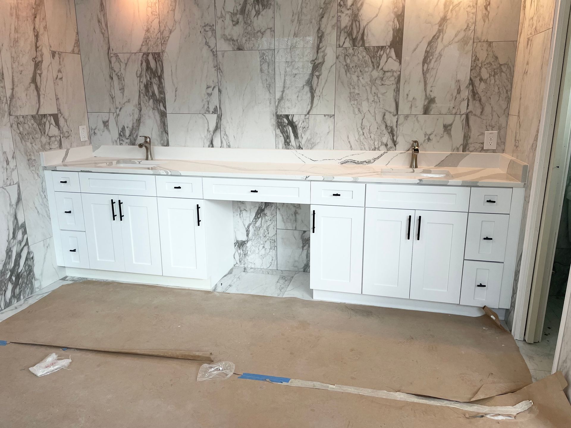 White double-sink bathroom vanity with marble backsplash and countertop in a room under construction with floor paper.