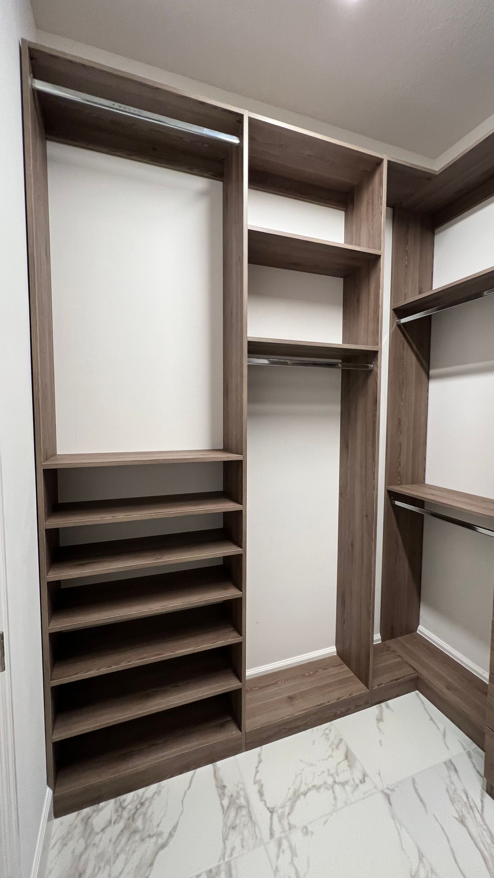 A modern walk-in closet with dark wood shelving, hanging rods, and a white marble floor.