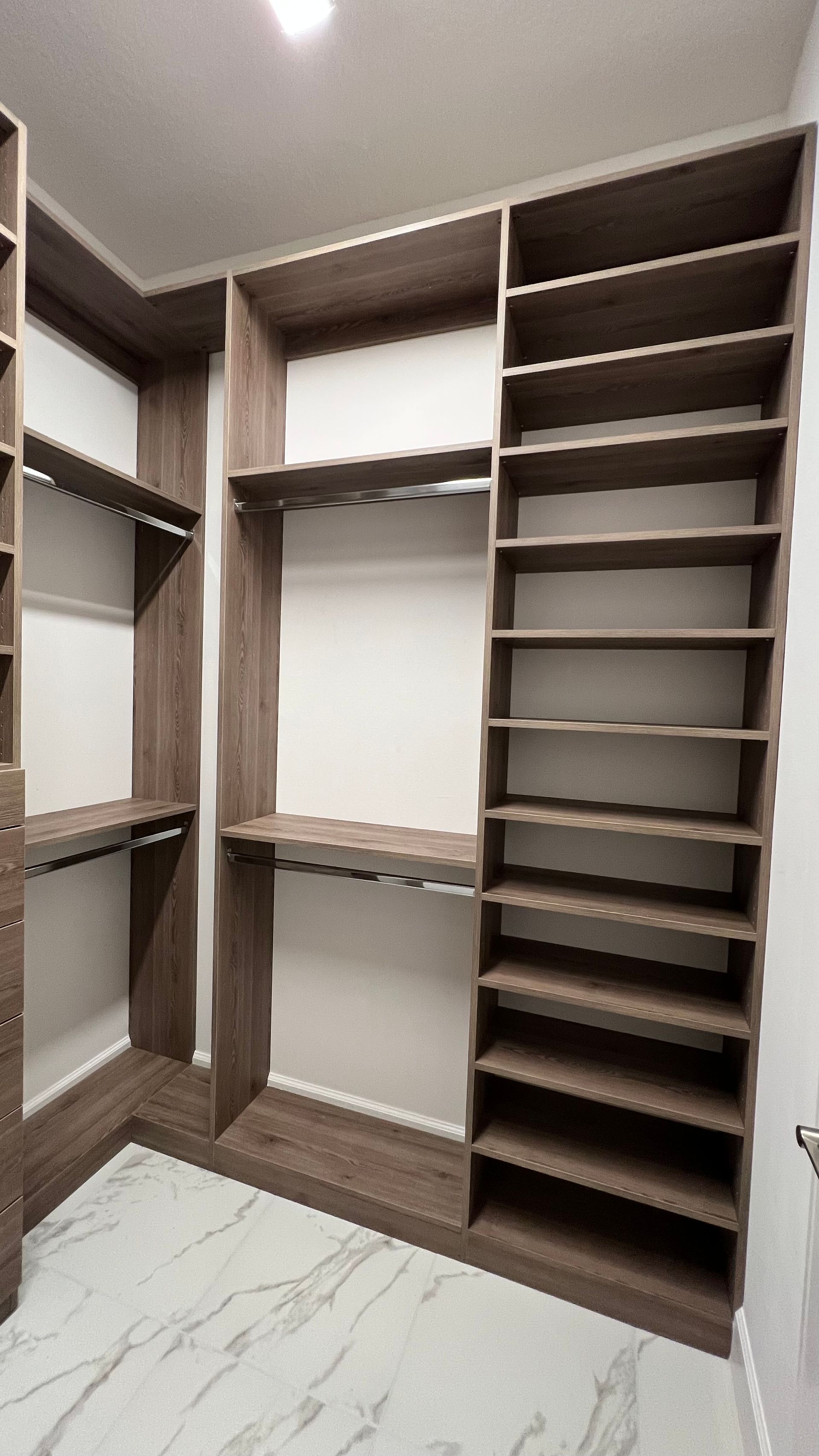 Empty, modern walk-in closet with dark wood shelves and a hanging rod over a white marble floor.