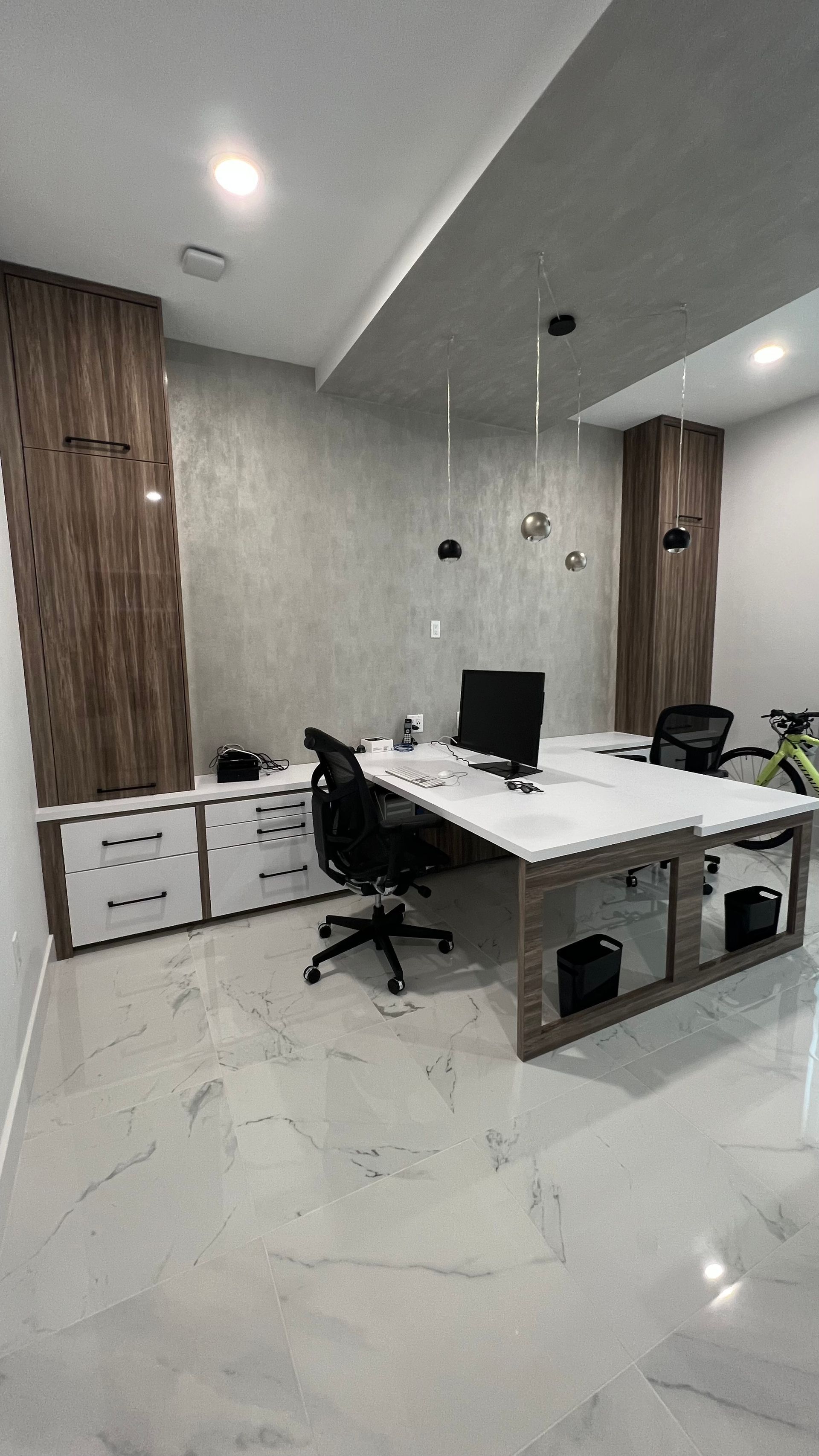 Modern office with a large white double desk, black chairs, white marble floor, and wood-paneled accent walls.