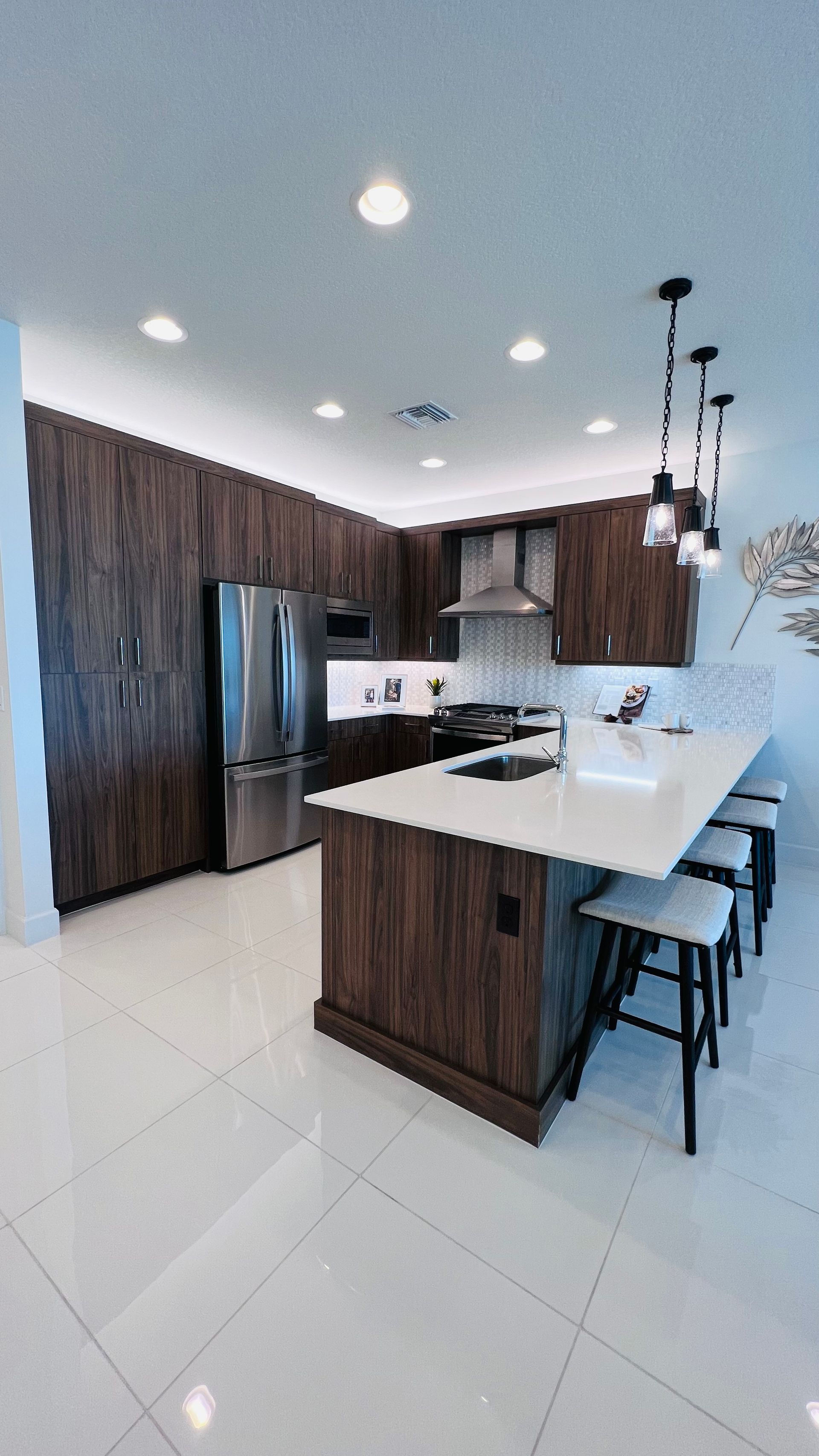 Modern kitchen with wood cabinets, white countertops, stainless steel appliances, and three pendant lights over an island.