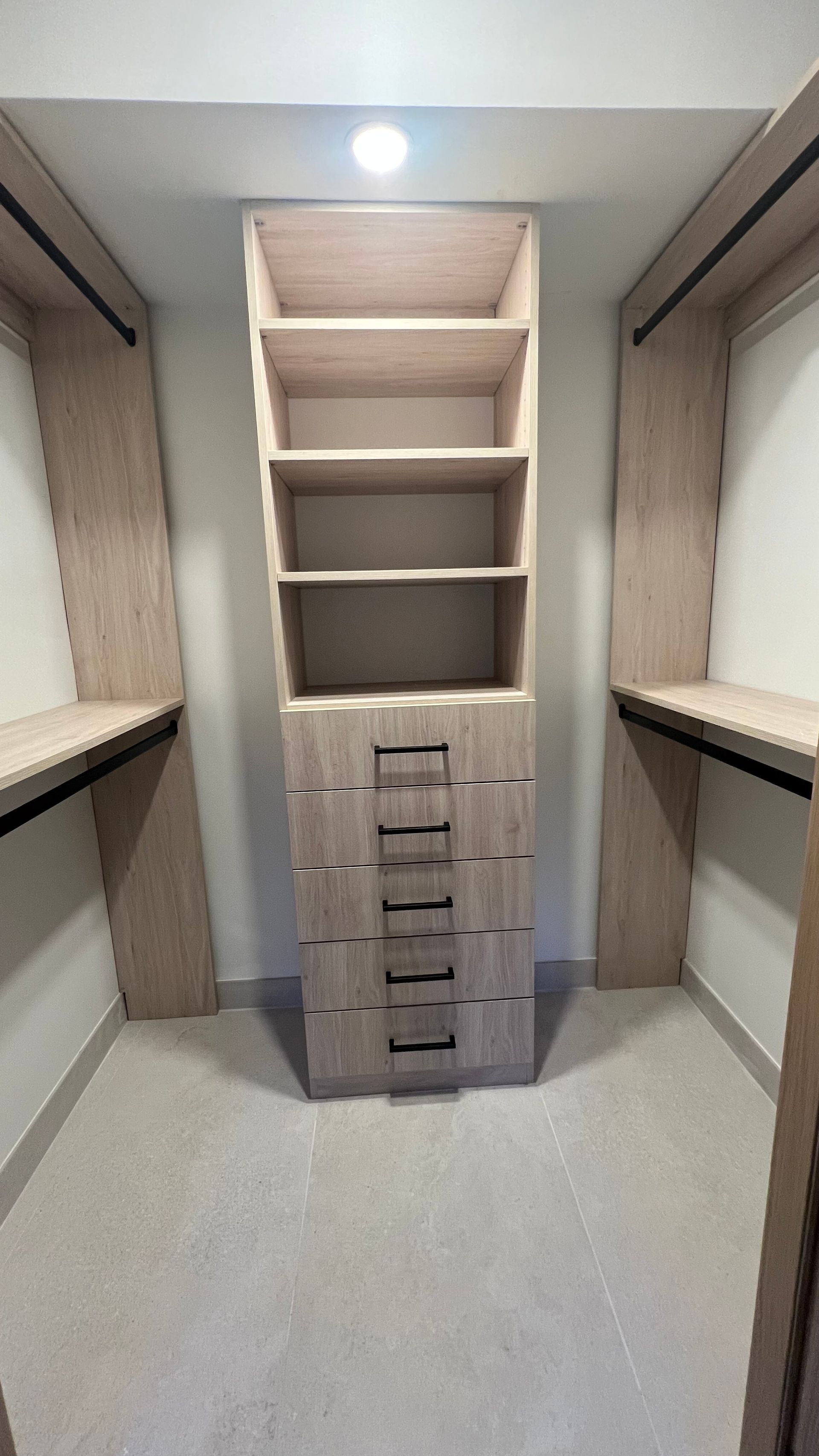 A reach-in closet featuring light wood-grain shelves and a central drawer stack between two hanging rods.