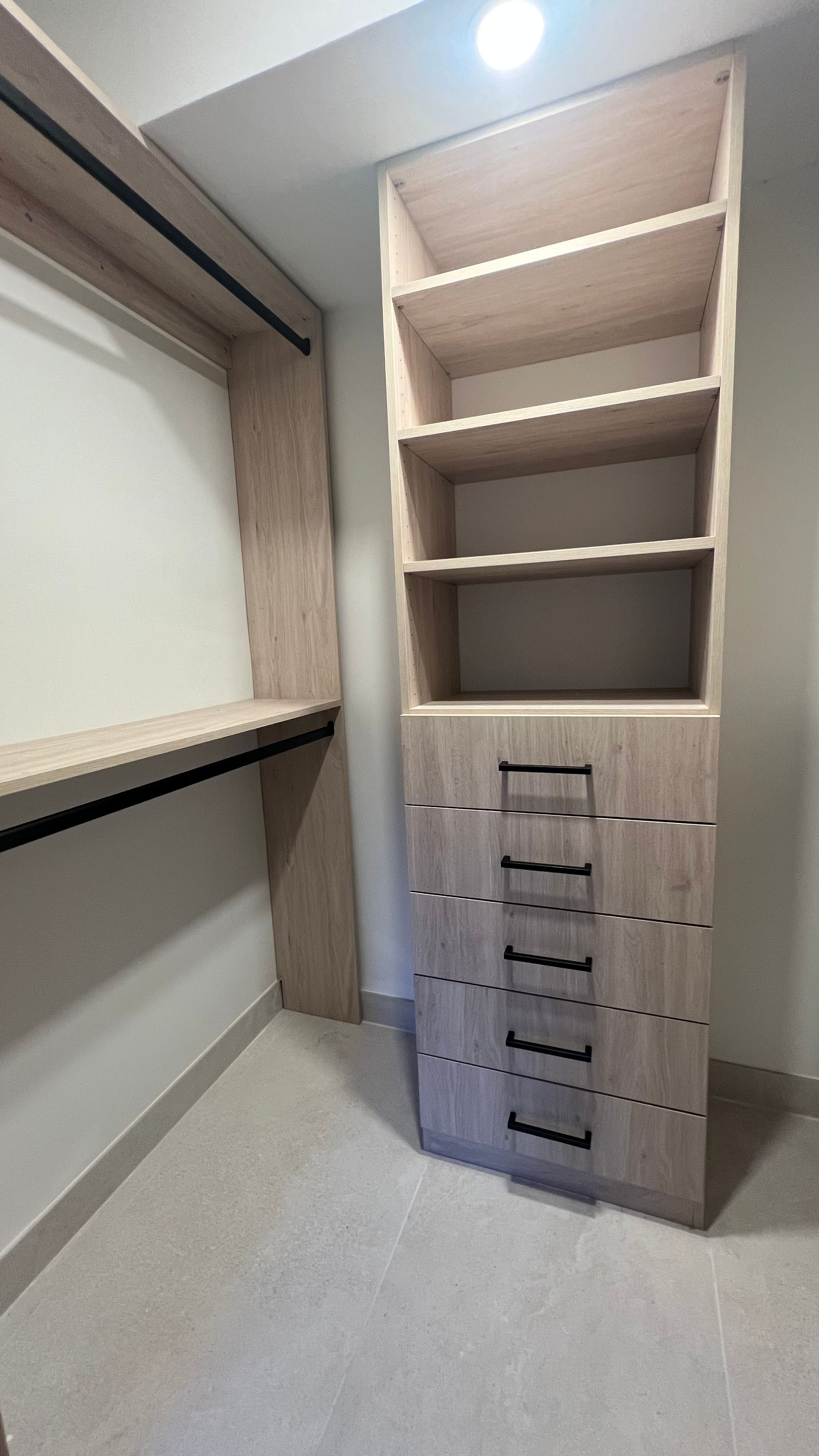 A light wood walk-in closet featuring a tall unit with five drawers and open shelving, next to a hanging rod section.