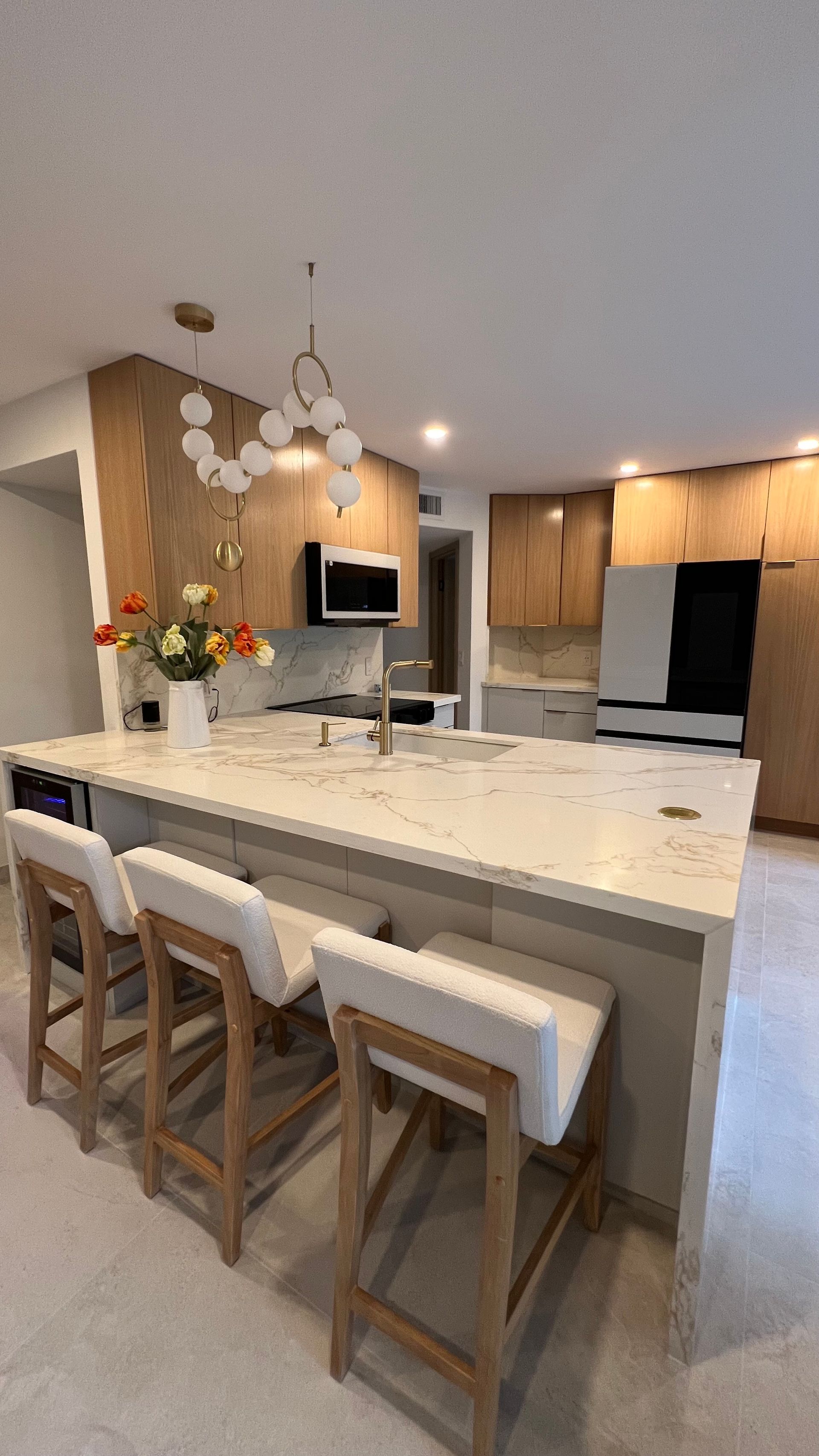A modern kitchen features a large white marble island with three light-colored stools beneath a cluster pendant light.