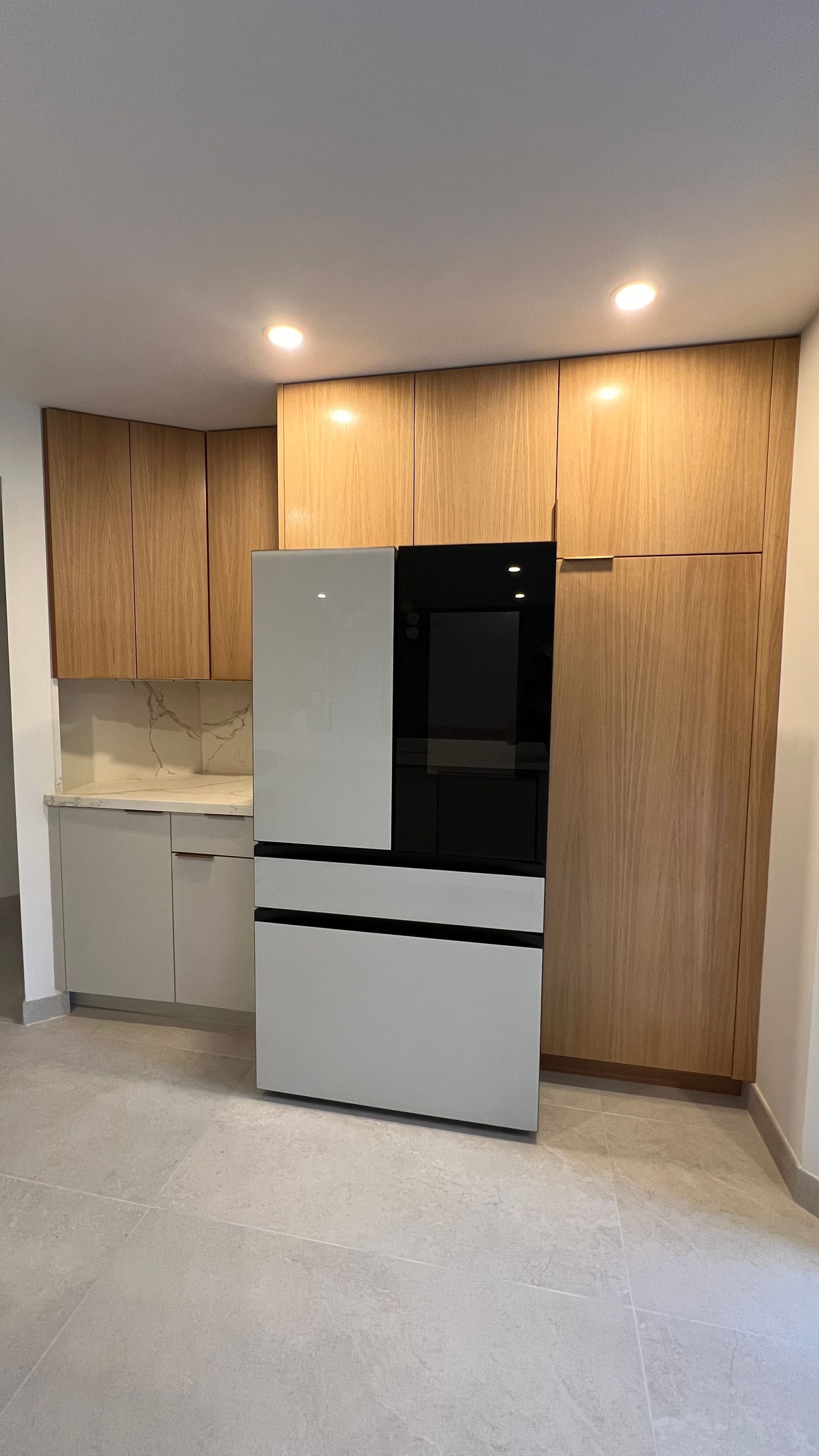 A modern kitchen featuring a light wood cabinetry wall with a large, two-toned grey and black refrigerator.