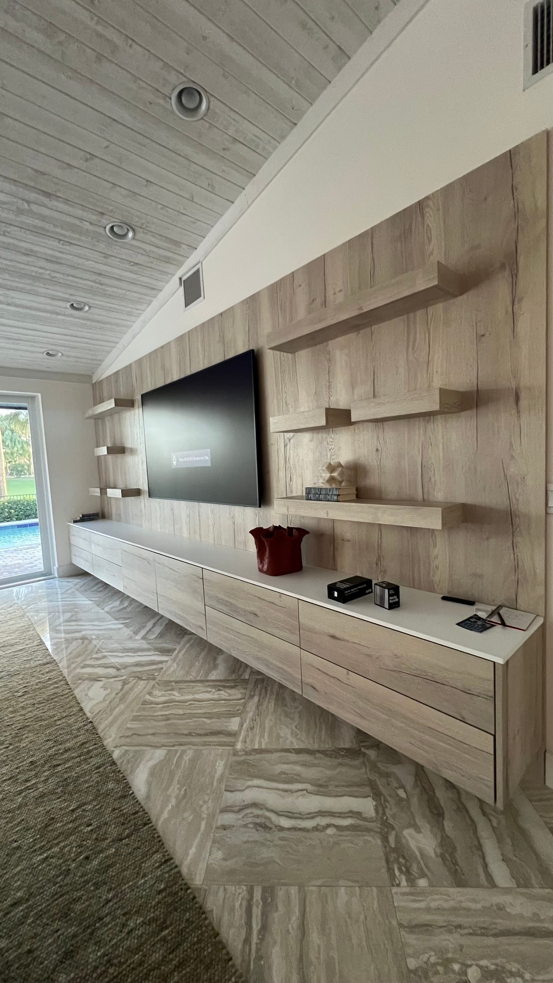 A wide shot of a modern living room featuring a long, light wood floating media console with a TV and wall-mounted shelves.