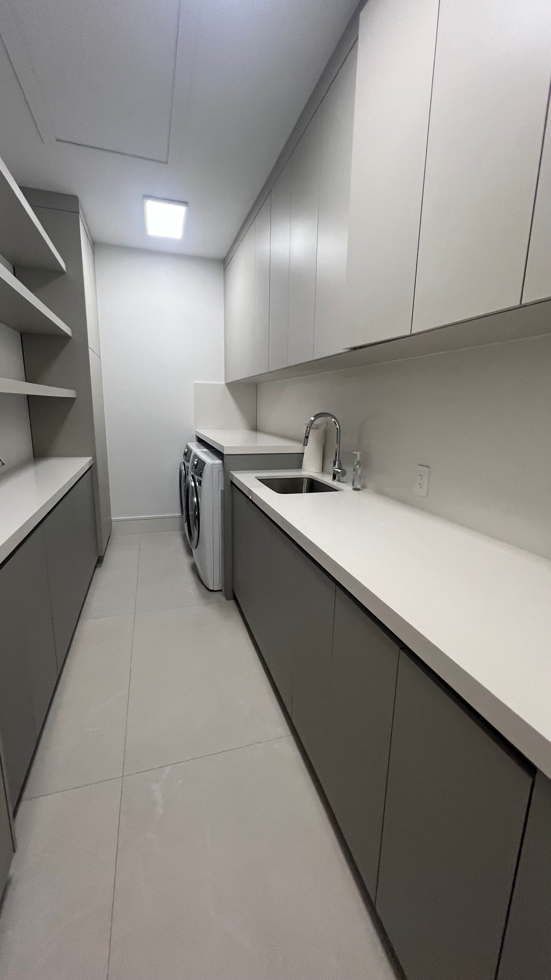 Modern laundry room with gray base cabinets, white countertops, upper cabinets, a sink, and a washer-dryer unit.