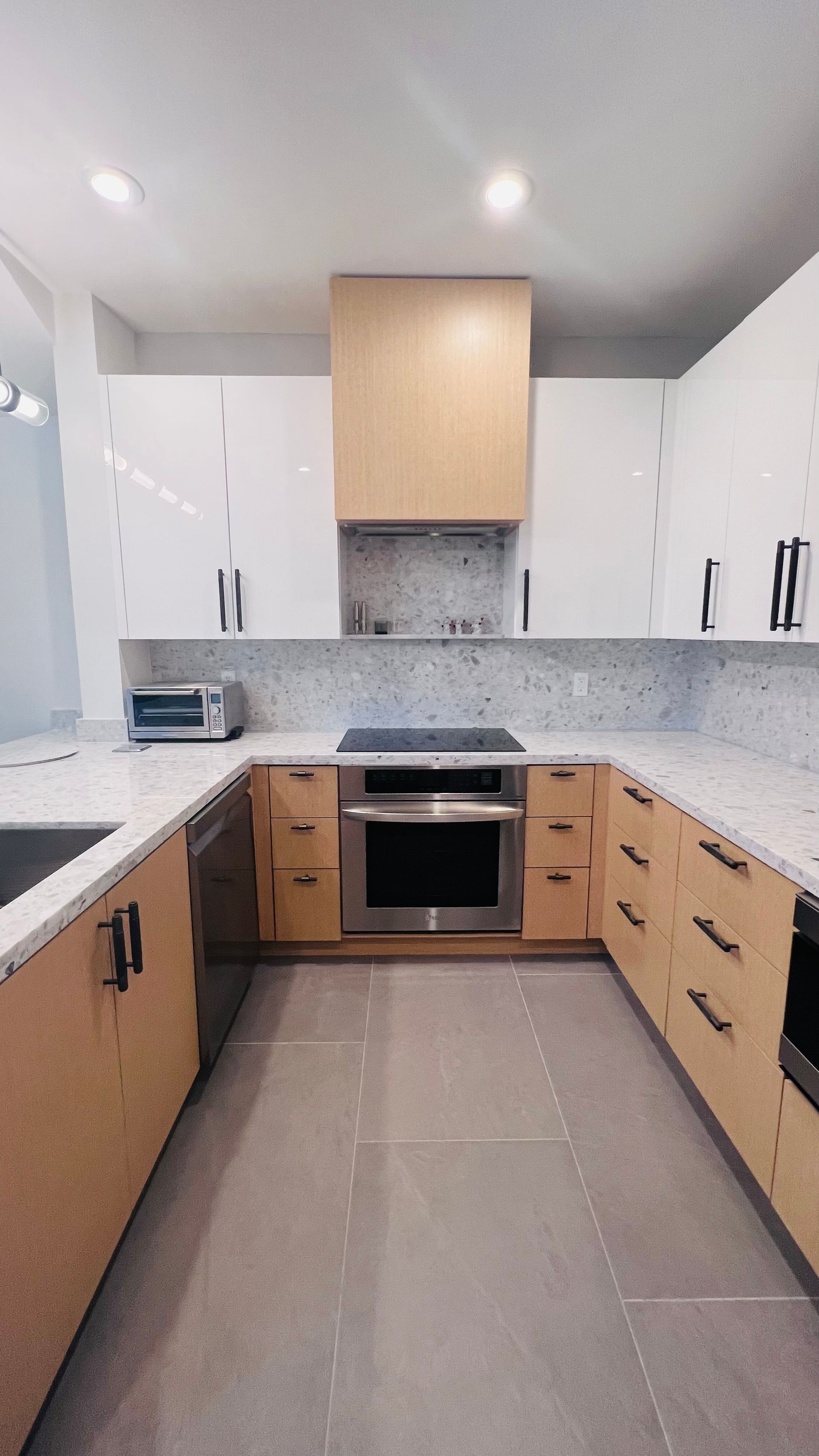 A U-shaped kitchen with light wood lower cabinets, white upper cabinets, stainless steel appliances, and a tile backsplash.