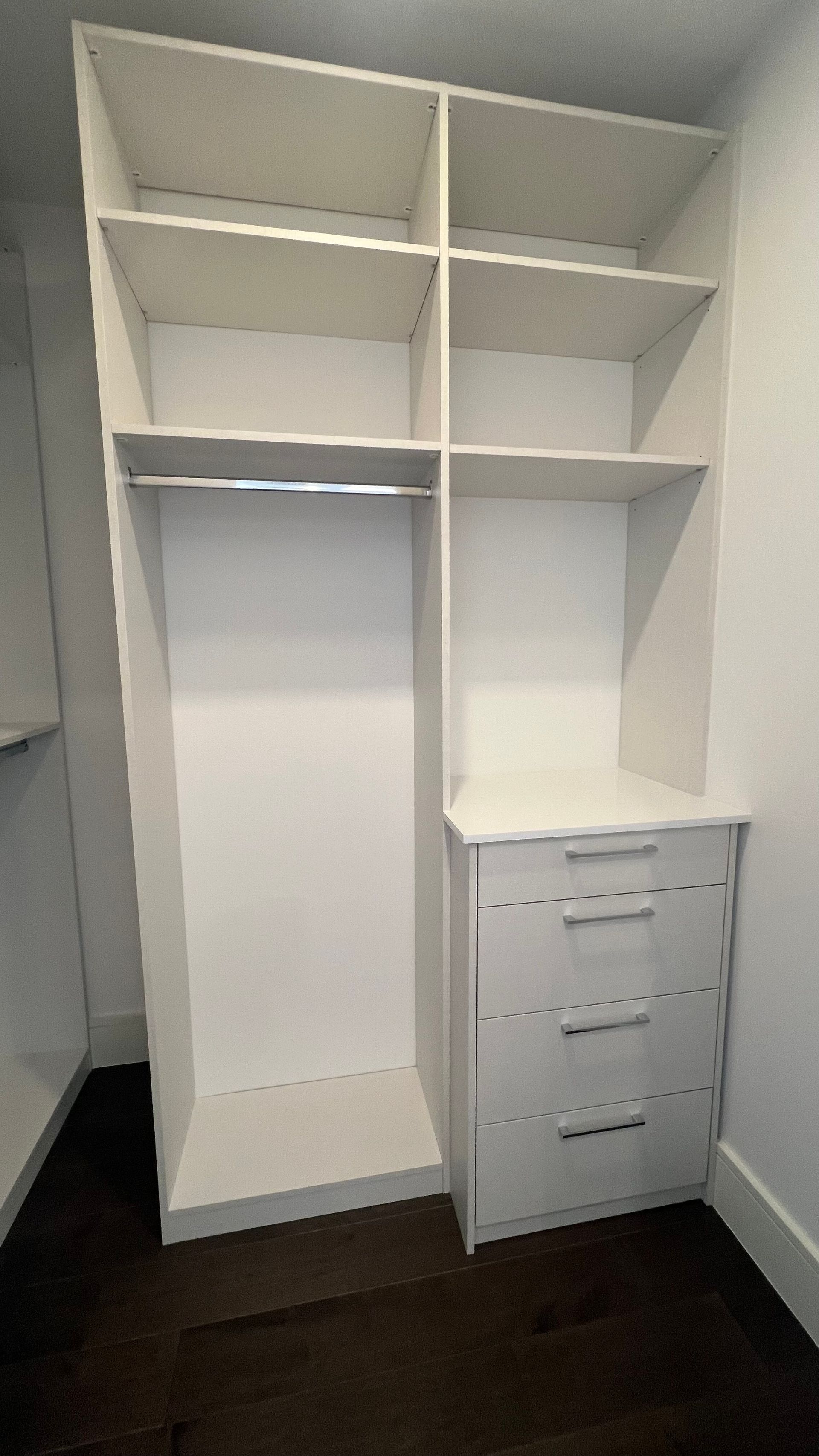 A white reach-in closet with an upper shelf, a hanging rod on the left, and three drawers on the right.